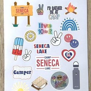 May include: A collection of colorful stickers featuring camp-themed designs, including a peace sign, a campfire, a rainbow, a smiley face, a popsicle, a s'more, a water bottle, and a sign that reads "Camp Seneca Lake".