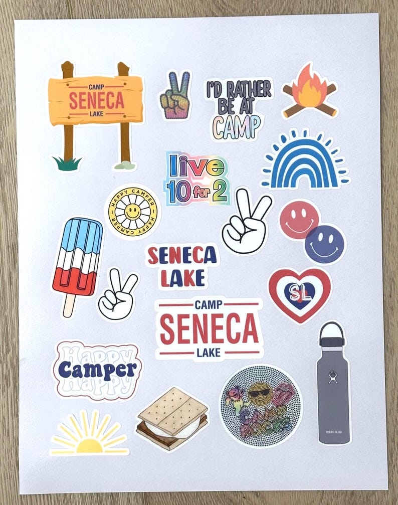 May include: A collection of colorful stickers featuring camp-themed designs, including a peace sign, a campfire, a rainbow, a smiley face, a popsicle, a s'more, a water bottle, and a sign that reads "Camp Seneca Lake".