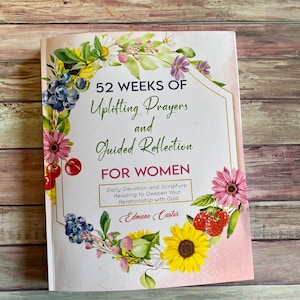 May include: A pink book with a floral design on the cover. The title is "52 Weeks of Uplifting Prayers and Guided Reflection for Women". The subtitle is "Daily Devotion and Scripture Reading to Deepen Your Relationship with God". The author's name is "Edmane Castor".