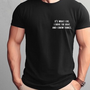 May include: Black t-shirt with white text that reads "It's what I do. I drive the boat and I know things."