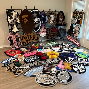 May include: A collection of various tufted rugs in diverse shapes, colours, and designs, including sports team logos like the Lakers, Rams, and Saints, character motifs such as Hello Kitty, Stitch, and Bratz, and brand logos like Supreme and Roblox.