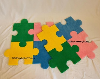 May include: A set of five puzzle pieces made of soft fabric. The pieces are in the colours yellow, green, blue, and pink. The pieces are arranged in a puzzle shape. The text "madhavluxuryhous" is printed on two of the pieces.