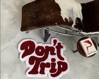 Puede incluir: Una alfombra blanca y roja con las palabras "Don't Trip" en una fuente retro.