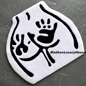 May include: White, uniquely shaped rug with a black handprint and abstract design. The rug has a soft, textured surface and is likely made of a plush material. The text "MadhavLuxuryHouse" is visible on the rug.