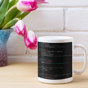 May include: White ceramic mug with a black background featuring Java code for a CoffeeMug class. The code includes variables for color, capacity, and current coffee level. The mug is a great gift for programmers and coffee lovers.