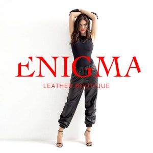 May include: A woman wearing a black bodysuit and black leather pants with a drawstring waist. She is wearing black heeled shoes and black leather gloves. The text "ENIGMA LEATHER BOUTIQUE" is displayed in red letters.