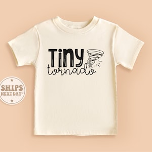 May include: A white short-sleeved t-shirt with black text that reads "Tiny tornado" and a black illustration of a tornado.