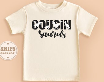 May include: A white t-shirt with black text that reads "COUSINsaurus" with dinosaur silhouettes forming the letters.
