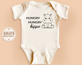 May include: White baby onesie with a black and white illustration of a hippopotamus and the text "HUNGRY HUNGRY hippo".
