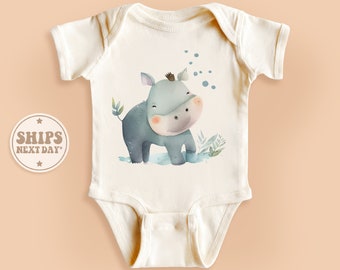May include: A white baby onesie with a cute cartoon illustration of a gray hippopotamus with blue eyes and a pink nose. The hippo is standing in a green grassy area with blue bubbles around it.