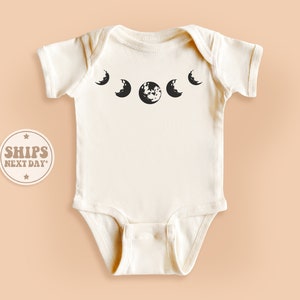 May include: A white baby onesie with a black moon phase design. The design features five moons in different phases, including a full moon.