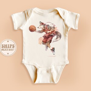 May include: A white baby onesie with a graphic print of a wolf playing basketball. The wolf is wearing a red jersey and shorts. The basketball is orange.