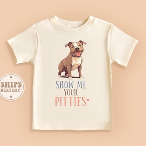 May include: White t-shirt with a brown and white pit bull terrier illustration and the text "Show Me Your Pitties" in blue and pink.
