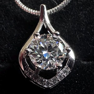 May include: A silver pendant necklace with a large, clear, round gemstone set in a silver frame. The frame has a delicate, openwork design.