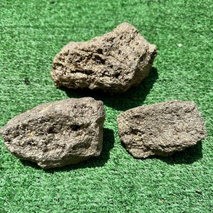 Pode incluir: Três peças de mineral de pirita bruto com tons metálicos e uma textura rugosa, porosa e cristalina. Cada pedra apresenta uma forma irregular e dentada com uma superfície de cor cinza e dourado fosco, exibindo formações minerais naturais.