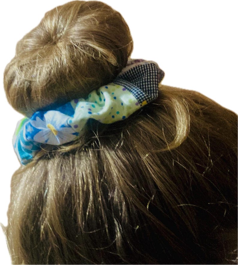 K&ouml;nnte beinhalten: Ein farbenfrohes Haargummi mit Blumen- und Tupfenmuster umwickelt einen Dutt aus braunem Haar. Das Haargummi hat einen Stoff mit blauen, wei&szlig;en und gelben Blumen sowie einen Abschnitt aus schwarz-wei&szlig; kariertem Stoff.