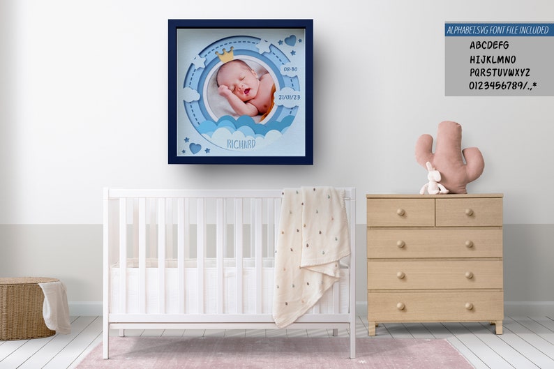 May include: A framed baby photo in a nursery setting. The blue-framed artwork features a sleeping baby with a crown, clouds, and the name "Richard." The text "ALPHABET.SVG FONT FILE INCLUDED" is visible. A white crib, dresser, and decorative items are also in the room.