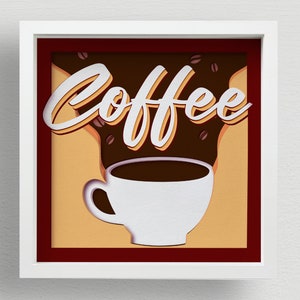 Könnte beinhalten: Ein weiß gerahmtes Bild mit einem roten Passepartout. Das Bild zeigt ein Papier-Cut-Out-Design einer Kaffeetasse mit aufsteigendem Dampf. Der Dampf ist in Form des Wortes "Coffee" geformt.