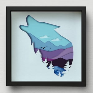 May include: A paper cut-out art piece in a black frame. The silhouette of a wolf howling at the moon is cut out, revealing a landscape of mountains, trees, and a lake. The colors are blue, purple, and green.