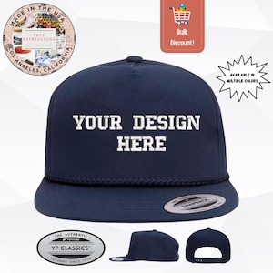Könnte beinhalten: Marineblaue Snapback-Kappe mit dem weißen Text "YOUR DESIGN HERE". Die Kappe hat einen flachen Schirm und ein Seildetail. Zusätzliche Ansichten der Kappe sind abgebildet. Die Kappe ist von YP Classics.