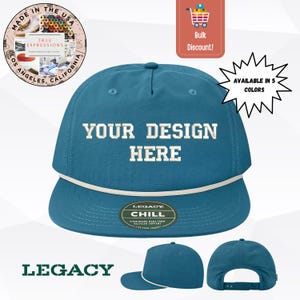 Può includere: Cappellino da baseball color teal con la scritta bianca "YOUR DESIGN HERE". Il cappellino ha un dettaglio in corda bianca e una visiera piatta. Sono visibili anche le scritte "LEGACY" e "AVAILABLE IN 5 COLORS".