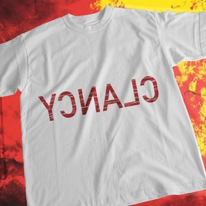 May include: White t-shirt with the word "CLANCY" printed in red on the front.