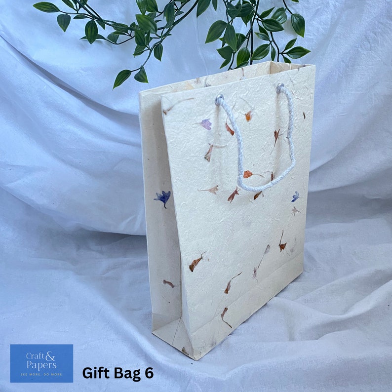 May include: A white gift bag with a white rope handle. The bag is made of textured paper with a floral pattern in shades of brown, orange, and blue. The bag is labeled "Gift Bag 6".