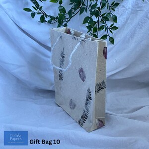 May include: A white gift bag with a floral design and a white rope handle. The bag is made of recycled paper and has a natural, rustic look. The text "Gift Bag 10" is printed on the bottom of the bag.