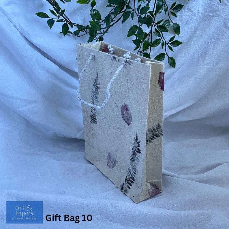 May include: A white gift bag with a floral design and a white rope handle. The bag is made of recycled paper and has a natural, rustic look. The text "Gift Bag 10" is printed on the bottom of the bag.