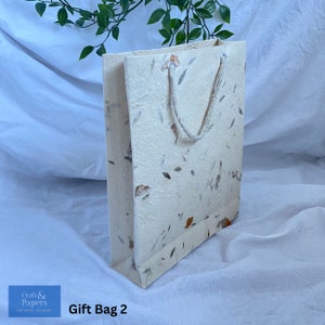 May include: A white gift bag with a floral pattern and a white rope handle. The bag is made of recycled paper and has a natural, rustic look. The text "Gift Bag 2" is printed on the bottom of the image.