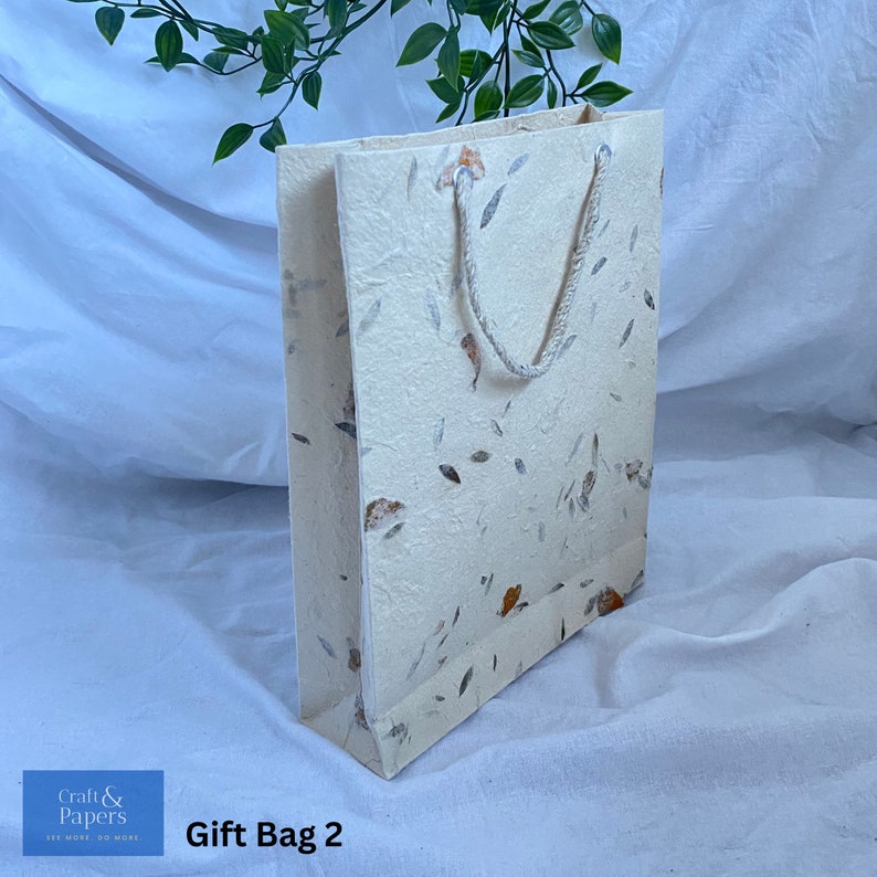 May include: A white gift bag with a floral pattern and a white rope handle. The bag is made of recycled paper and has a natural, rustic look. The text "Gift Bag 2" is printed on the bottom of the image.