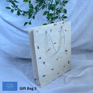 May include: A white gift bag with a floral pattern and a white rope handle. The bag is made of recycled paper and has the text "Craft & Papers" on the bottom left corner. The text "Gift Bag 3" is on the bottom right corner.