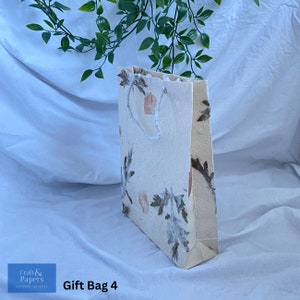 May include: A white gift bag with a floral design. The bag has a white rope handle and is made of recycled paper. The bag is labeled "Gift Bag 4".
