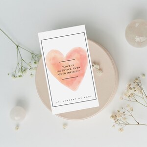 May include: A white card with a watercolor heart in shades of pink and orange. The card features the quote "Love is inventive, even onto infinity" and is attributed to St. Vincent de Paul.