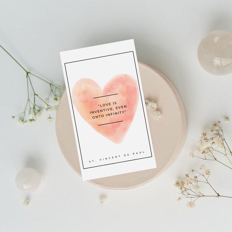 May include: A white card with a watercolor heart in shades of pink and orange. The card features the quote "Love is inventive, even onto infinity" and is attributed to St. Vincent de Paul.