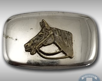 May include: Silver belt buckle with a horse head design. The horse head is made of brass and is set against a silver background.