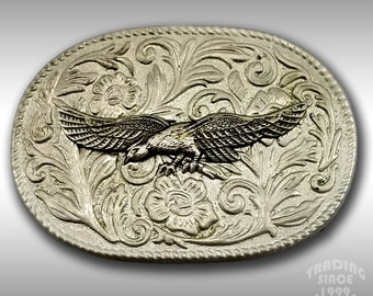 May include: Silver-toned belt buckle with an eagle design in the center. The eagle is in flight and has a detailed, textured design. The buckle is surrounded by a floral pattern.