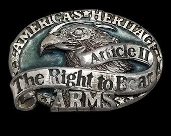 May include: Silver oval belt buckle with an eagle motif. The buckle is inscribed with the words "AMERICA'S HERITAGE" and "The Right to Bear ARMS". The text "Article II" is also visible on the buckle.