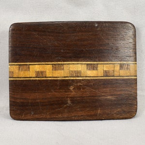 Puede incluir: Una hebilla de cinturón de madera marrón oscuro con una fina banda de madera clara incrustada en un patrón de cuadros.