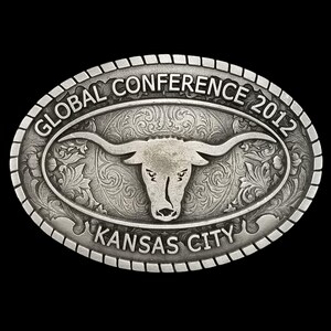 May include: Oval silver-toned belt buckle with a longhorn steer design. The buckle is engraved with the words "GLOBAL CONFERENCE 2012" and "KANSAS CITY". The background features a floral pattern.