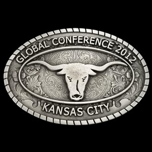 May include: Oval silver-colored belt buckle with a longhorn steer design. The buckle features the text "GLOBAL CONFERENCE 2012" and "KANSAS CITY" in a decorative font. The background has an ornate floral pattern.