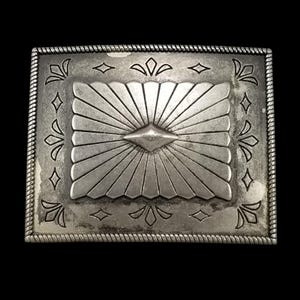 May include: A rectangular silver belt buckle with an ornate design. The centre has a sunburst pattern radiating from a diamond shape. The border is decorated with floral and diamond shapes, and a rope-like trim.