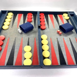 Op de afbeelding: Backgammon-spelset met een blauwe denim-achtige buitenkant. Het spelbord heeft rode, zwarte en grijze driehoeken, met gele en rode speelstukken. Inclusief dobbelstenen en blauwe dobbelbekers. Een klassiek bordspel.