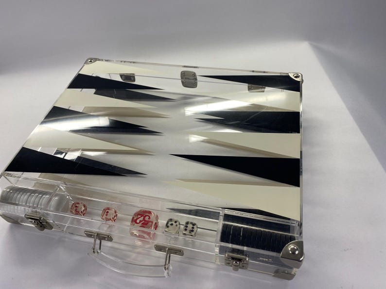 Pode incluir: Conjunto de backgammon em acr&iacute;lico transparente com um design geom&eacute;trico em preto e branco. O conjunto inclui dados vermelhos e brancos e uma caixa transparente com uma al&ccedil;a e fechos de metal. Um jogo de tabuleiro cl&aacute;ssico.