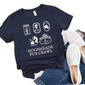 May include: A navy blue t-shirt with a white graphic of the Hogsmeade Pub Crawl. The graphic includes the names of five pubs: The Leaky Cauldron, The Three Broomsticks, Hog's Head, The Green Dragon, and The Shrieking Shack.