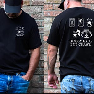 May include: Black t-shirt with a white graphic design featuring the text "Hogsmeade Pub Crawl" and illustrations of various pubs from the Harry Potter universe, including The Leaky Cauldron, The Three Broomsticks, and The Green Dragon.