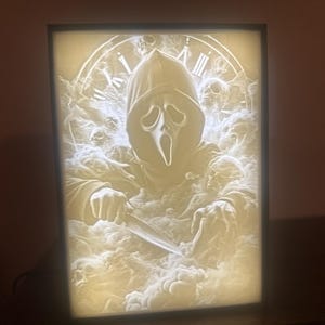 Puede incluir: Una decoración de pared iluminada en 3D impresa en blanco con el asesino Ghostface de la franquicia de películas Scream. La imagen muestra a Ghostface sosteniendo un cuchillo y rodeado de una nube de humo.
