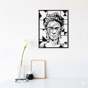 May include: Black metal wall art of a woman's face in a line drawing style, set against a geometric background. The artwork is displayed on a white wall above a table with a vase, candle, framed art, and spectacles.
