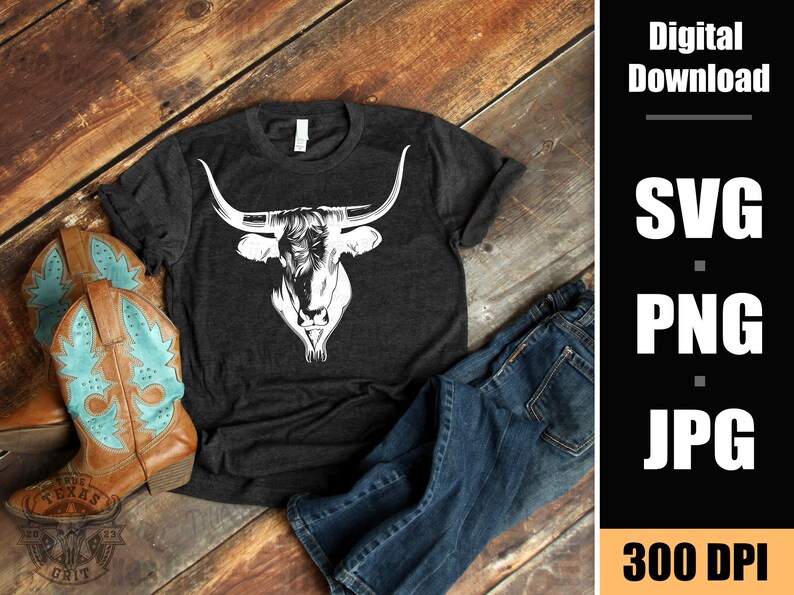 May include: A dark gray t-shirt with a white silhouette of a longhorn bull's head. The t-shirt is laying on a wooden surface with a pair of blue jeans and brown cowboy boots.