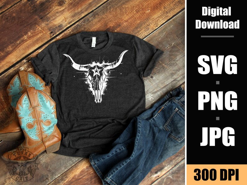 May include: A dark gray t-shirt with a white graphic of a stylized bull skull with a star in the center. The t-shirt is laying on a wooden surface with a pair of brown cowboy boots and blue jeans.